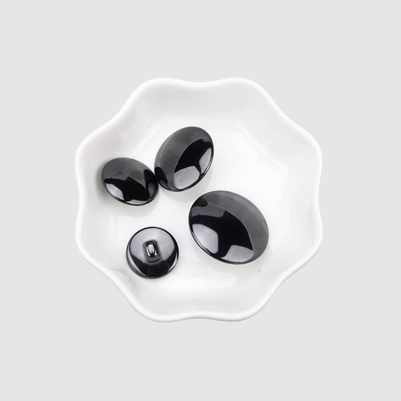 Black spherical ceramic buttons set in a dish, shank backs visible