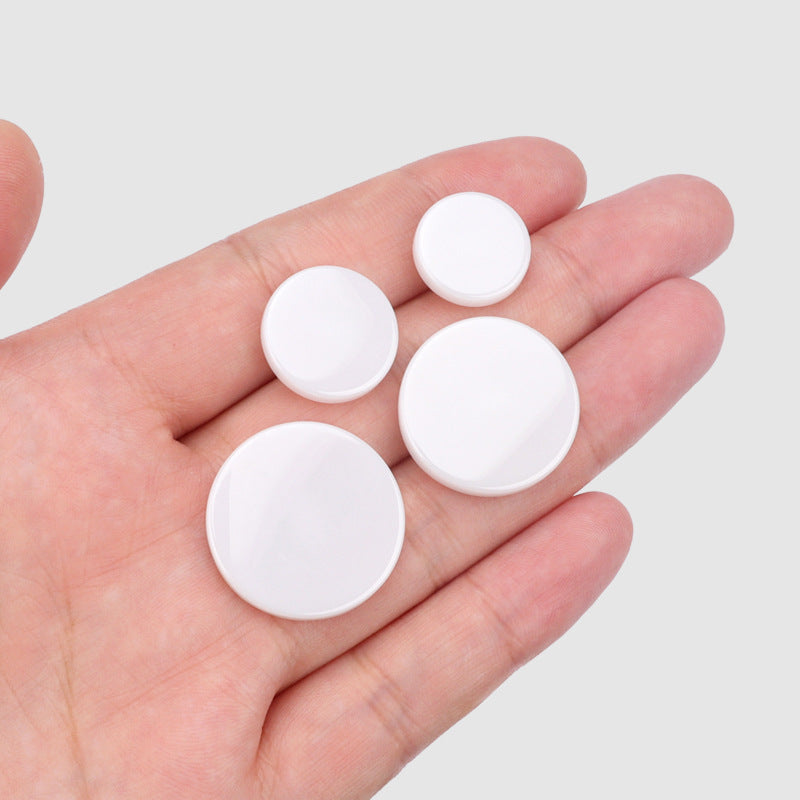 White ceramic flat buttons with shank, shown in hand, 15–25 mm