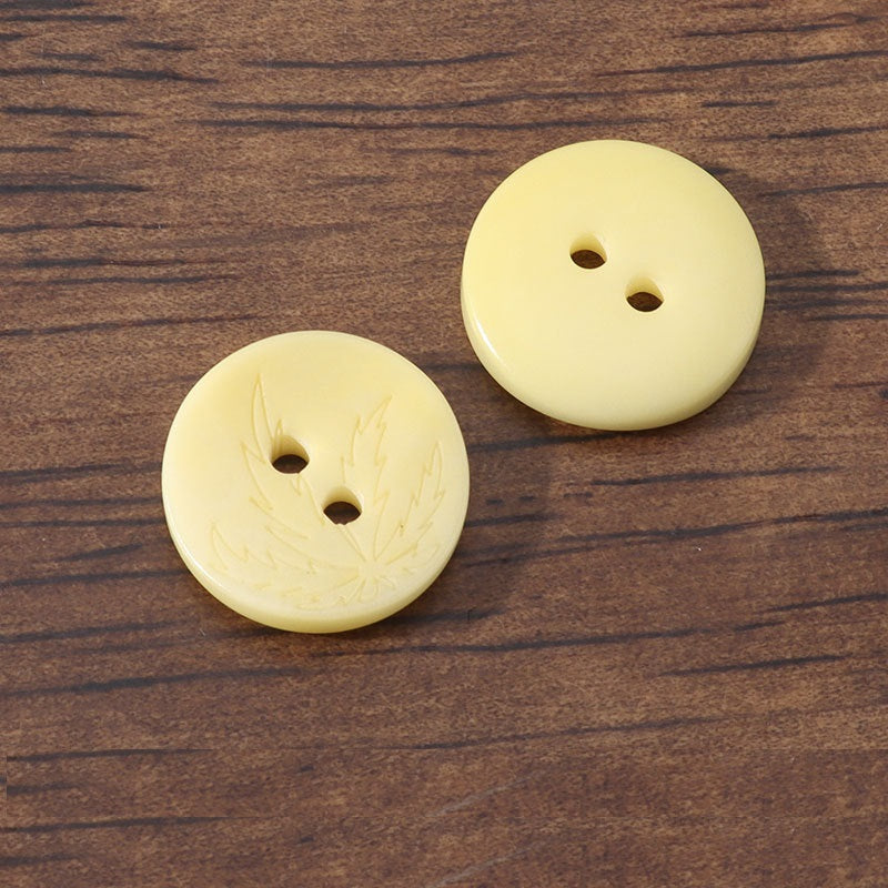 Yellow 2-hole corozo buttons with engraved leaf pattern, two pieces shown