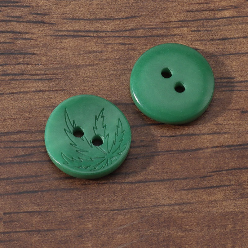 Green corozo buttons with 2 holes and laser-engraved leaf motif, two shown