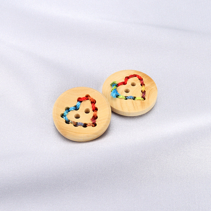 Two light-wood buttons with heart cutouts and red blue green stitched thread