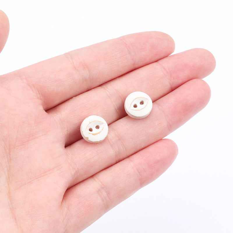 Round white 2-hole fish-eye buttons in hand, painted detail for crafts