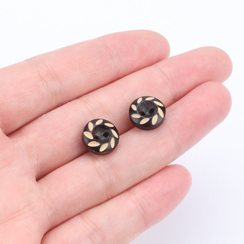 Two 11.5mm round wood buttons with leaf inlay, dark brown/black, shown in hand