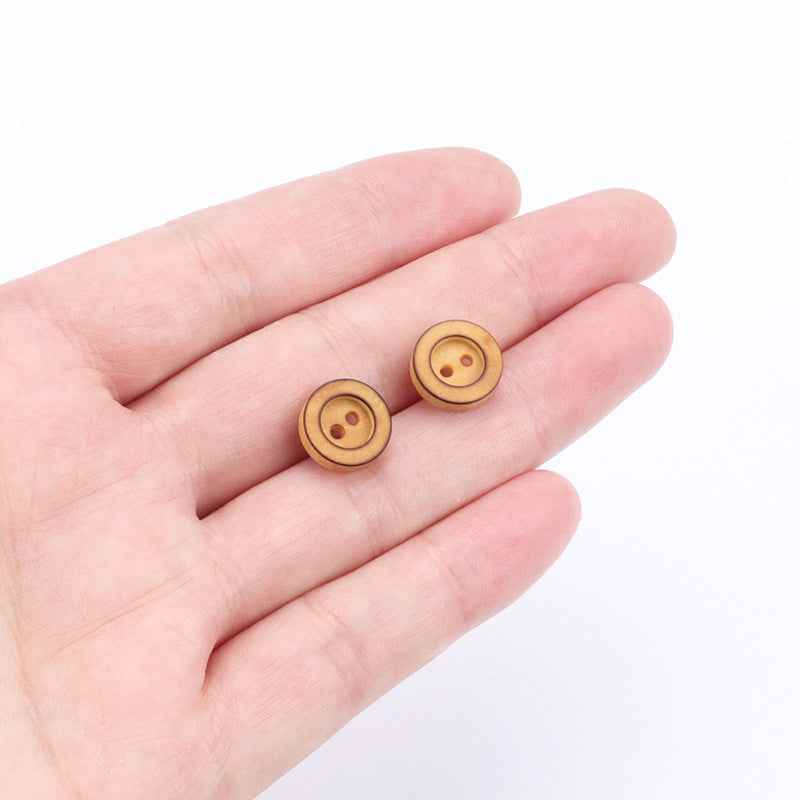 Two small round poplar wood buttons held in hand, tan, 2-hole front
