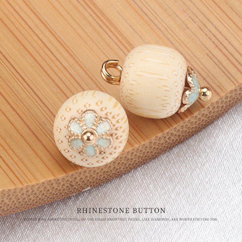 Cream bamboo frog knot button with gold flower setting and teal center stones, front view