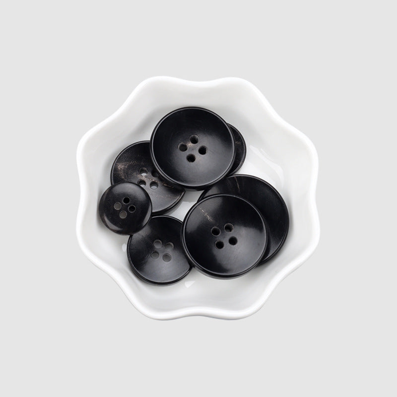 Set of black round horn buttons with 4 holes in a dish