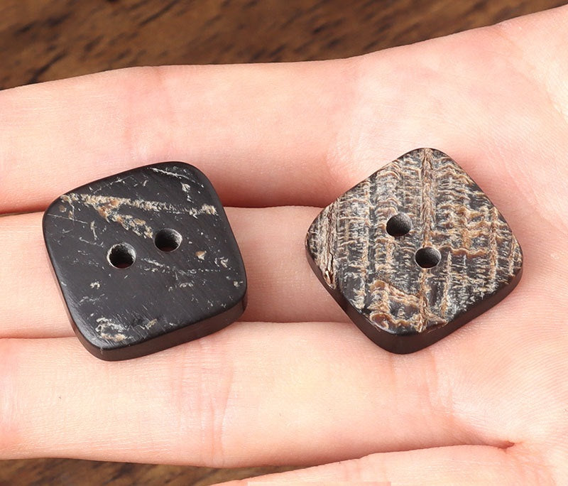 Pair of square 2-hole horn buttons, dark mottled patterns on hand
