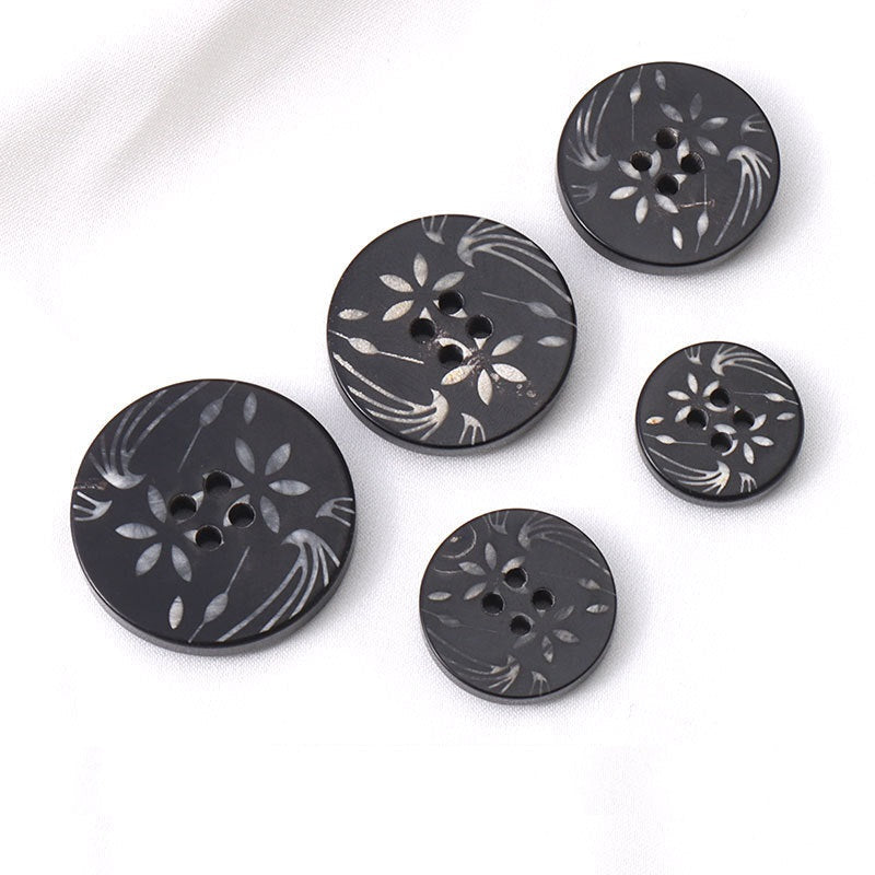 Five round black horn buttons with white floral pattern and 4-hole openings