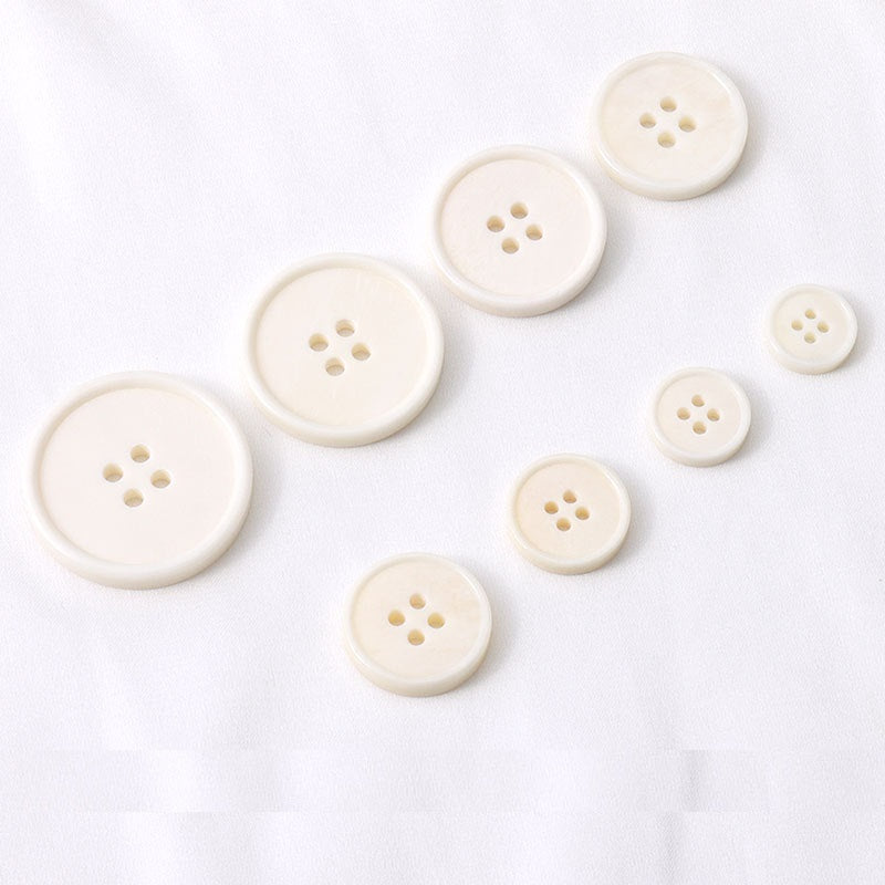 Multiple off-white 4-hole buttons, front view with four stitching holes