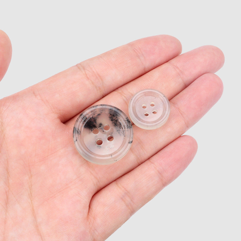 Two 18/25mm four-hole buttons in hand; translucent light blue with dark speckles