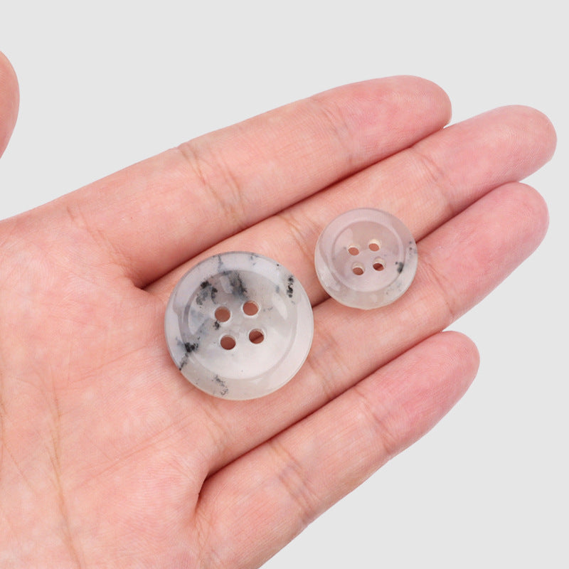 Two natural jade four-hole buttons in palm, speckled light blue-white