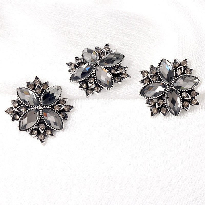 Three 23mm gunmetal-black floral rhinestone shank buttons with raised metal edging