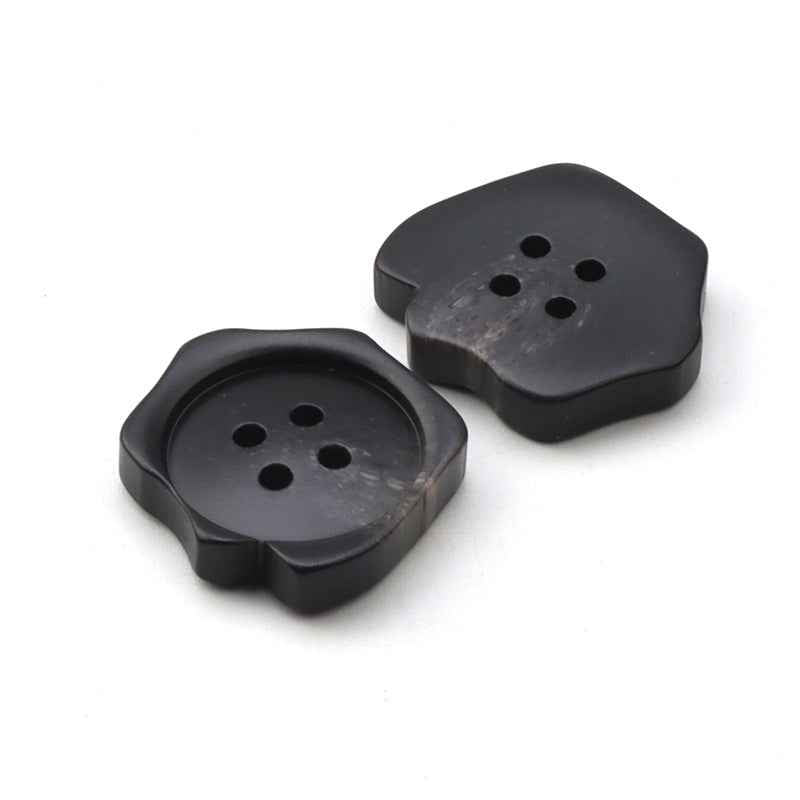 Black resin buttons with four holes, irregular rounded silhouette, angled view