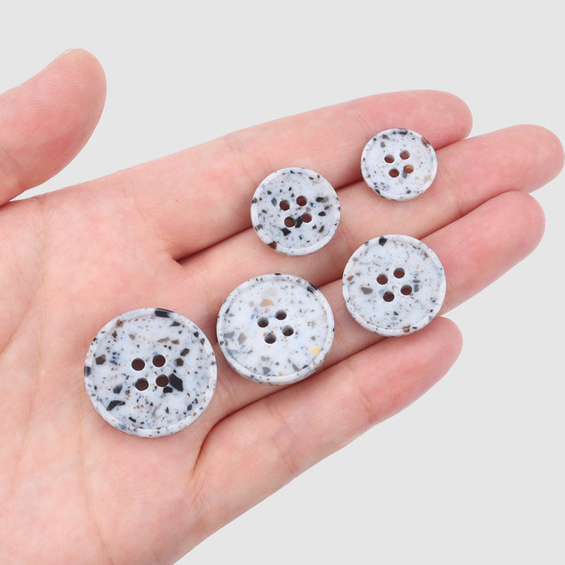 Multiple round marble-texture recycled resin buttons held in hand, 4 holes