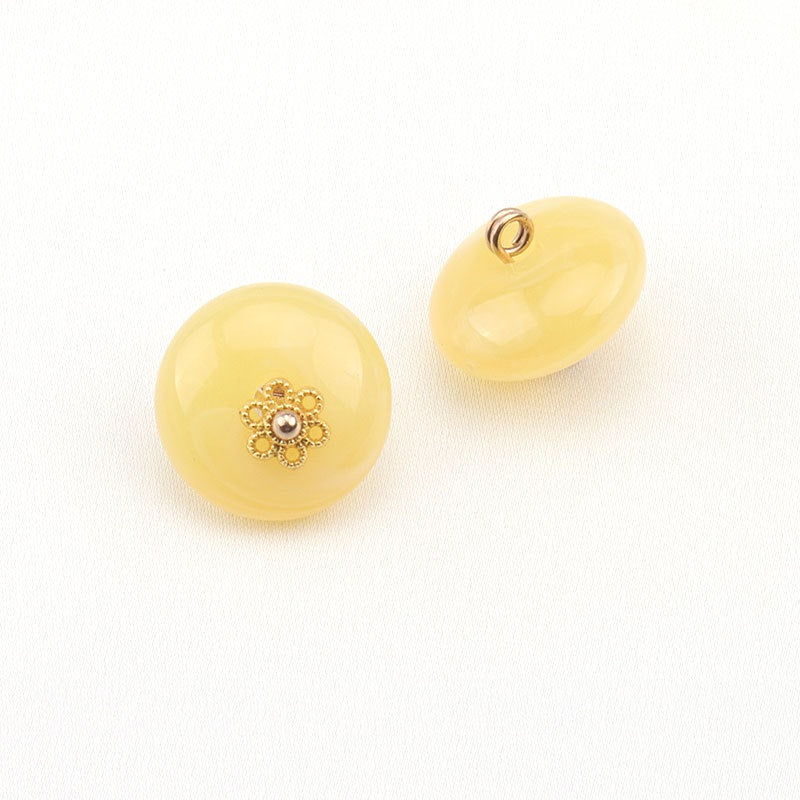Two pale yellow resin buttons; one shows gold floral with white center, other has metal loop