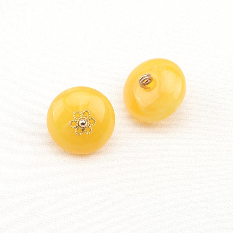 Pale yellow resin buttons: one gold floral with white center, one shows metal shank