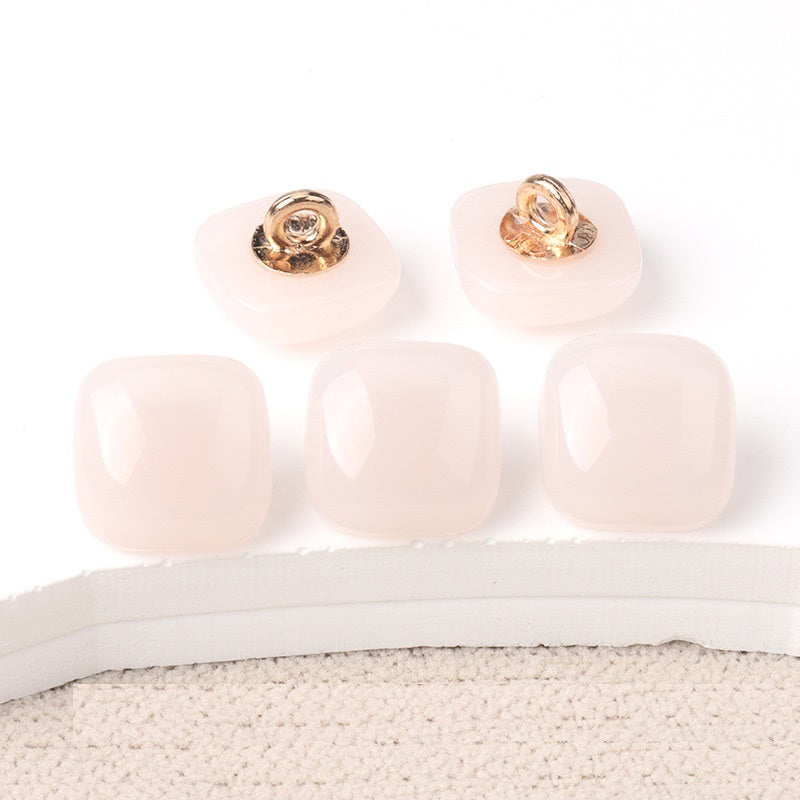 Blush pink square resin buttons with gold-tone shanks, glossy translucent finish