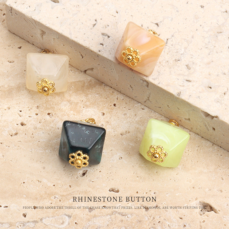 Four square acrylic buttons with gold rhinestone flower designs in pale tones and dark teal.