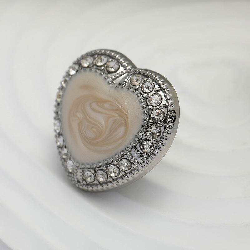 Heart-shaped metal button with white oiled center and rhinestone silver edge