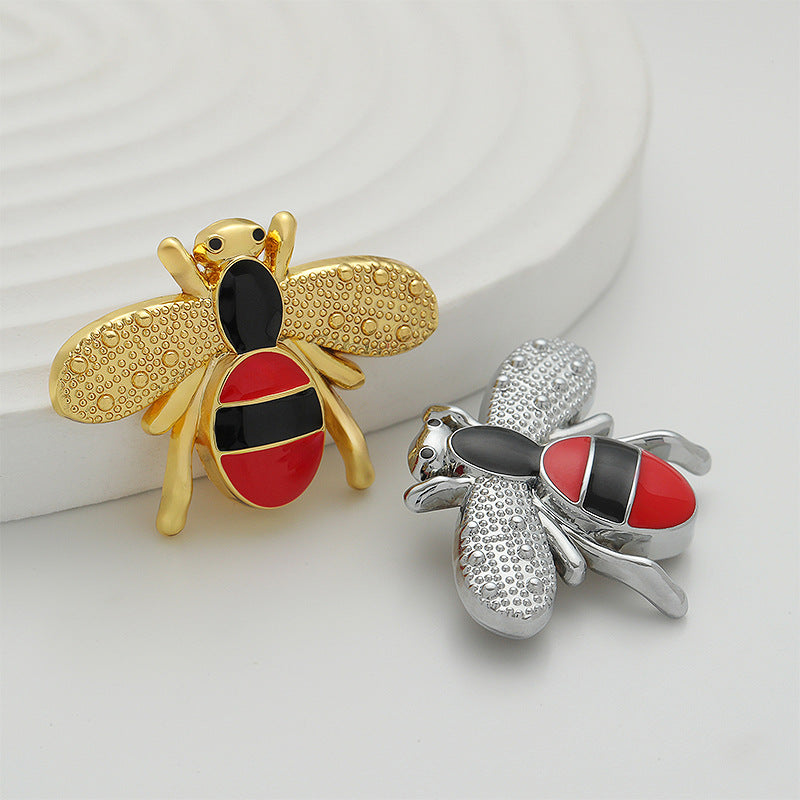Silver and gold bee-shaped metal brooches with red-and-black enamel details.