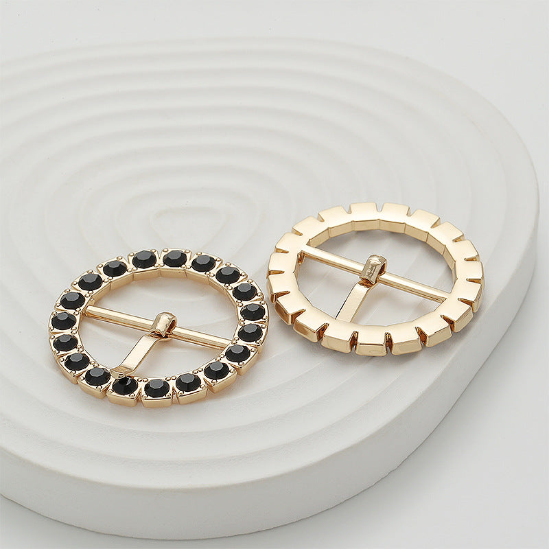 Two gold gear-shaped buckles with black stones on white display, back and front