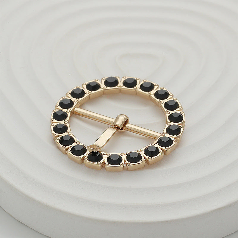 Gold gear-shaped metal buckle with black stones and bar pin closure, close-up
