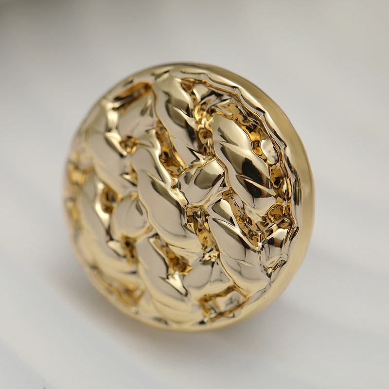 Gold round metal shank button with braided raised swirl pattern, close-up