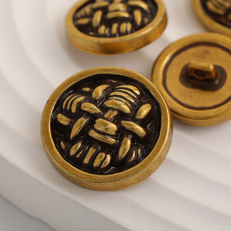 Close-up knot-shaped metal button, black face with gold relief pattern and rim