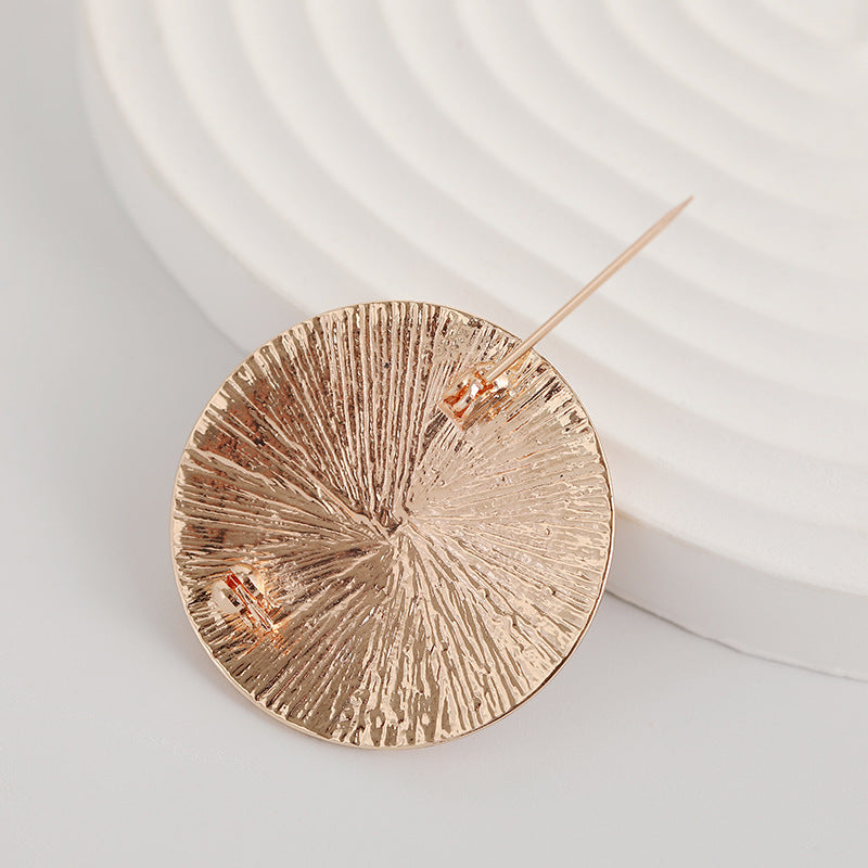 Gold-tone round metal brooch pin with textured swirl face and straight pin back