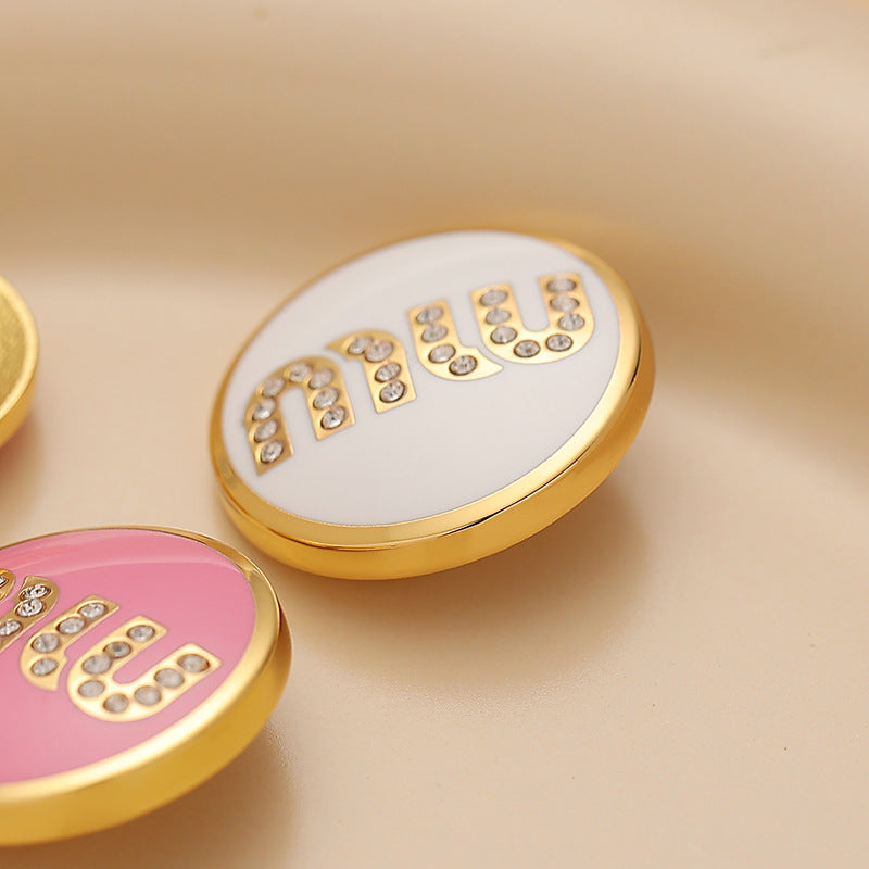 Close-up round metal sewing button, white lacquer MIU letters with rhinestones, gold rim
