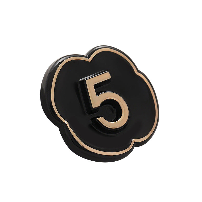 Black number 5 button with gold trim, glossy lacquer and raised “5” detail.
