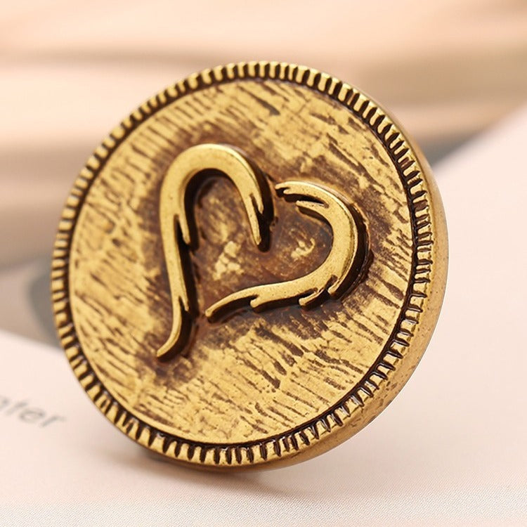 Close-up metal decorative button, light gold tone, heart engraved design