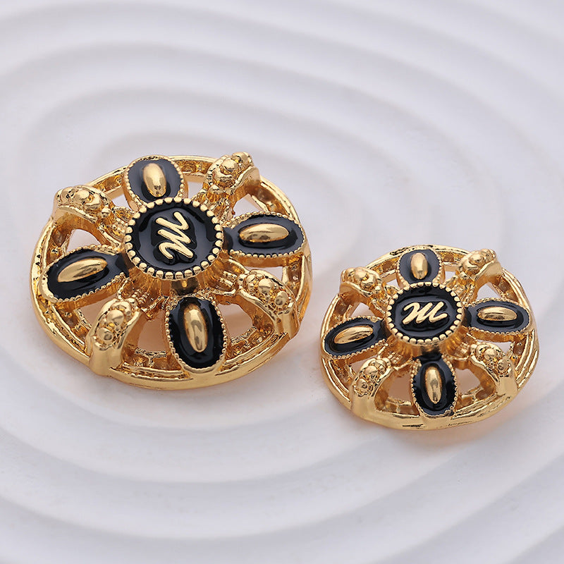 Two gold round hollow metal buttons with black letter M center and oval accents