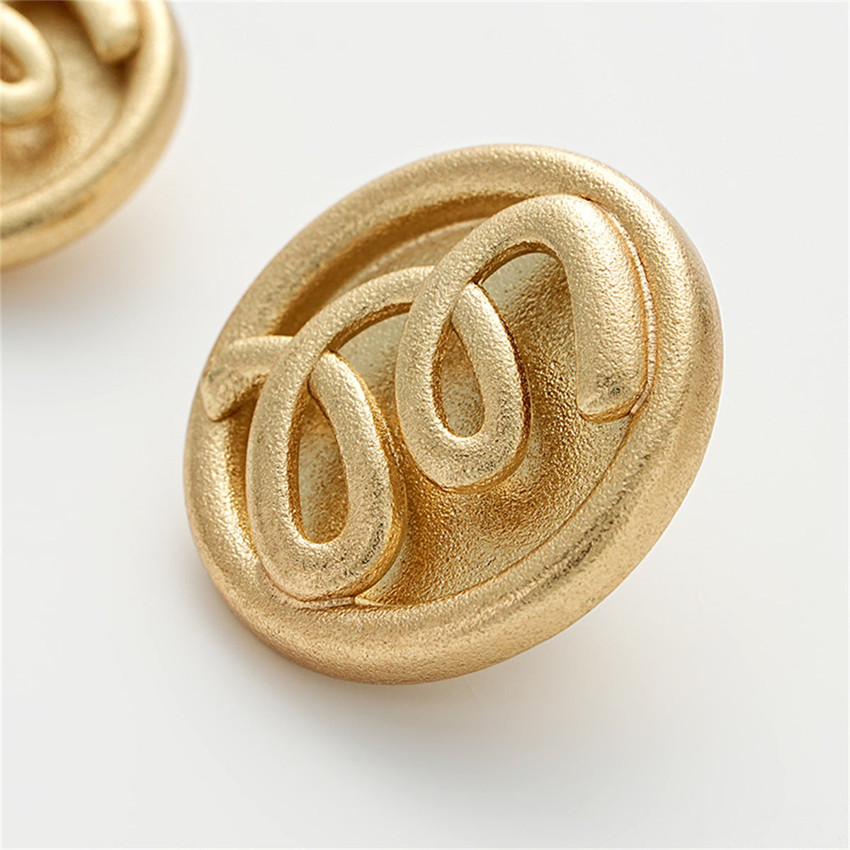 M letter embossed on sand-gold hollow metal button, side angle