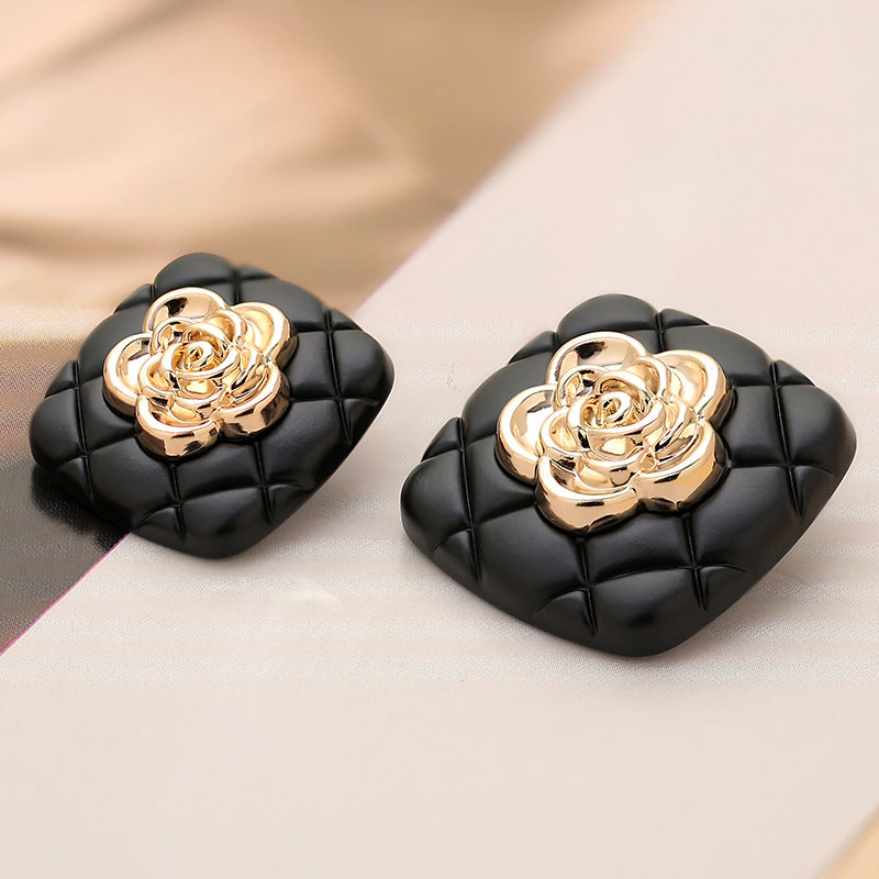 Pair of black square metal buttons with gold camellia centers on quilted grid