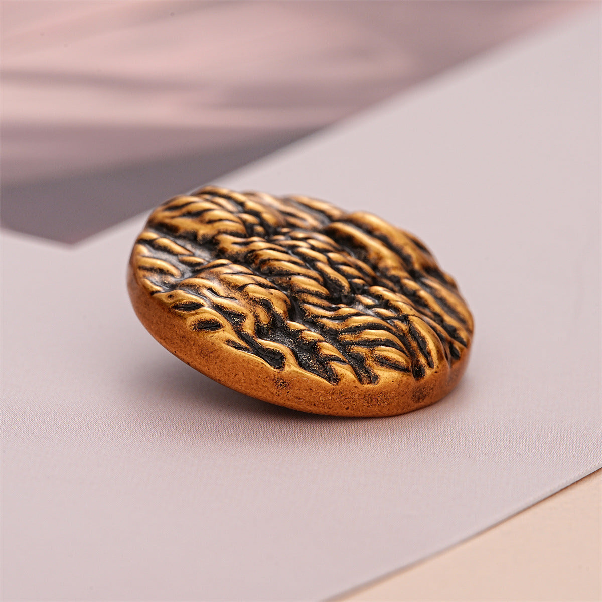 Black round metal button with gold striped texture on the front