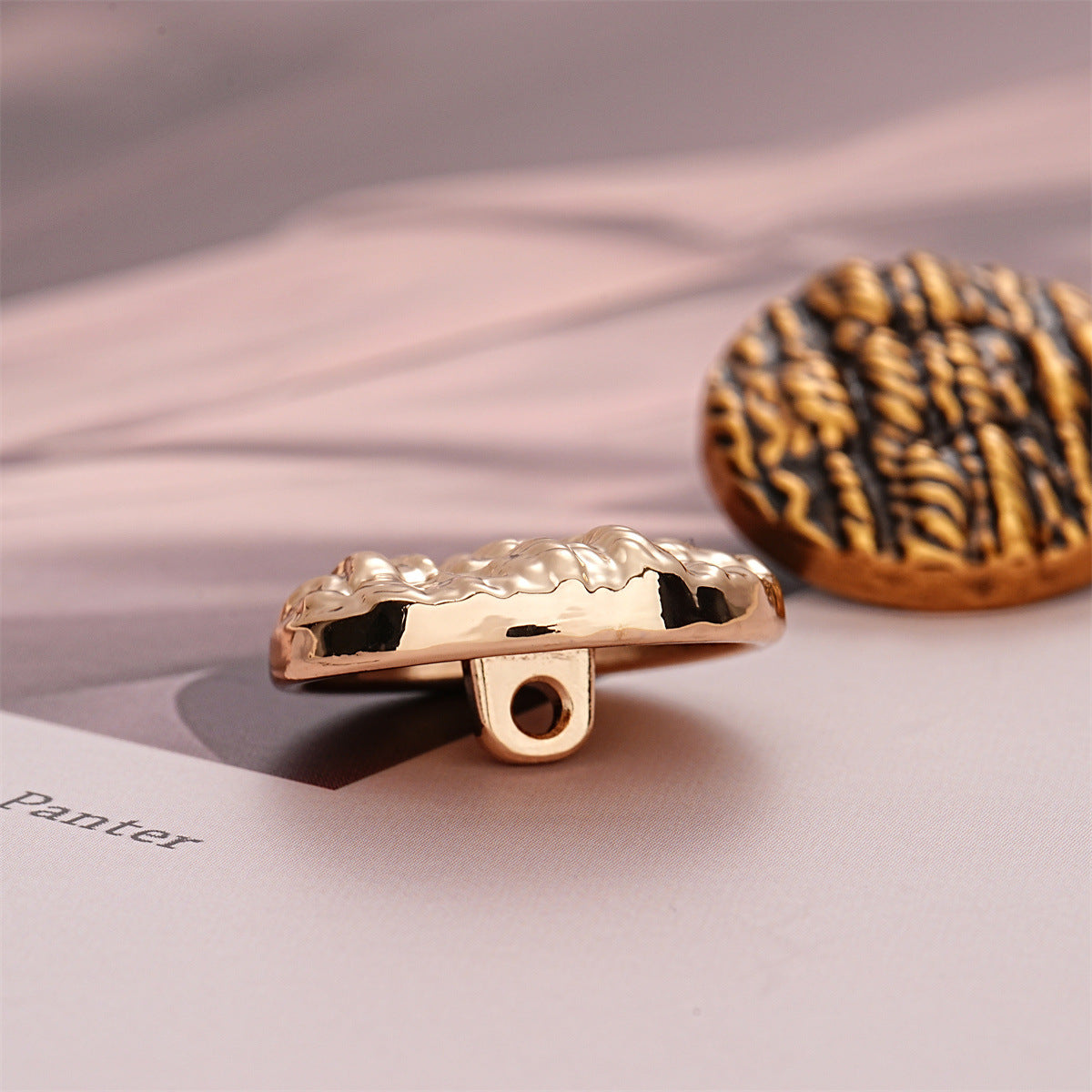 Rose gold round metal button with striped texture, showing shank underside