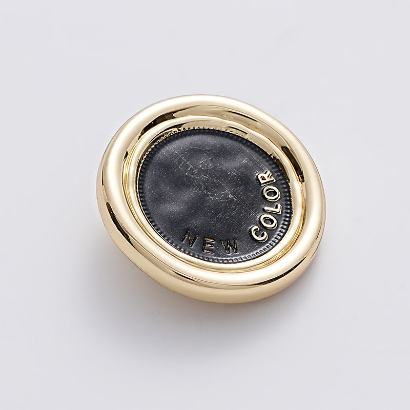 Black-gold two-tone round metal sewing button, dark center, handle loop visible.