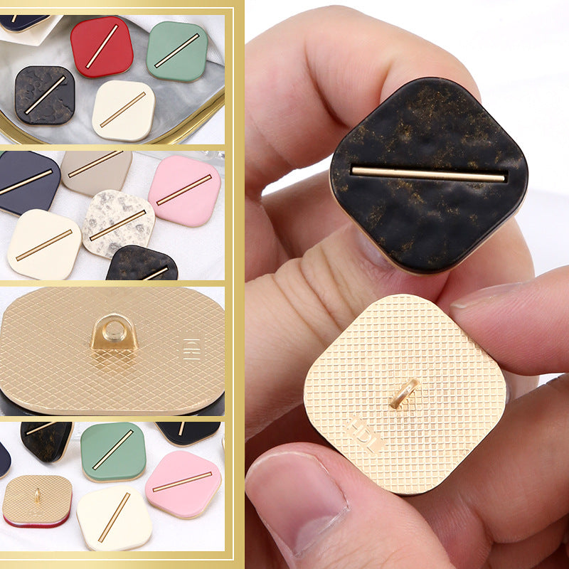 Hand holding rounded-square resin button with gold-tone bar, dark mottled color and light beige