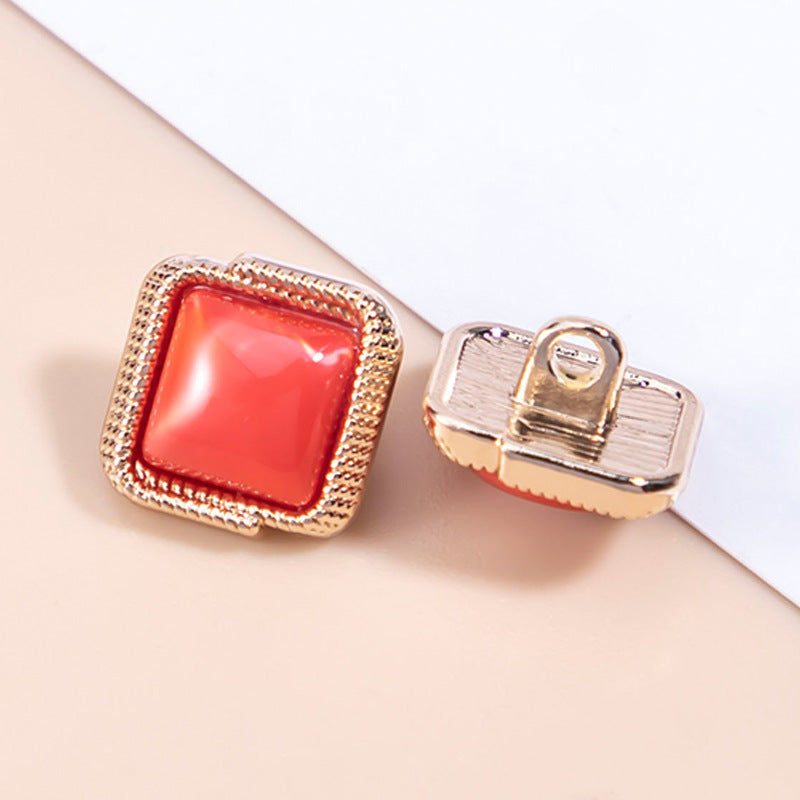 Red square resin button with shank and gold-tone frame; close-up side attachment