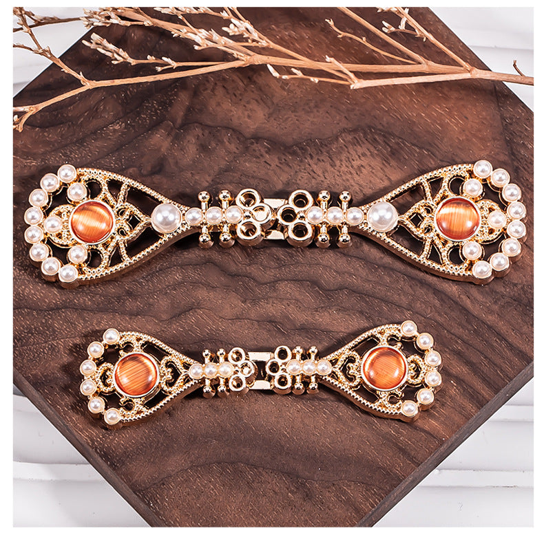 Close-up pipa-shaped metal buttons with orange cabochon and pearl border
