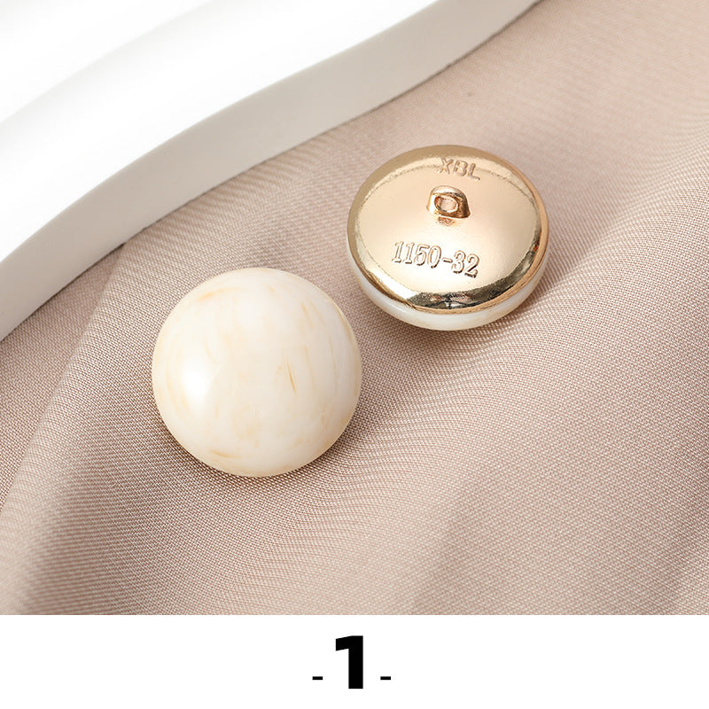 White cat’s eye resin button with gold metal base, back side facing up