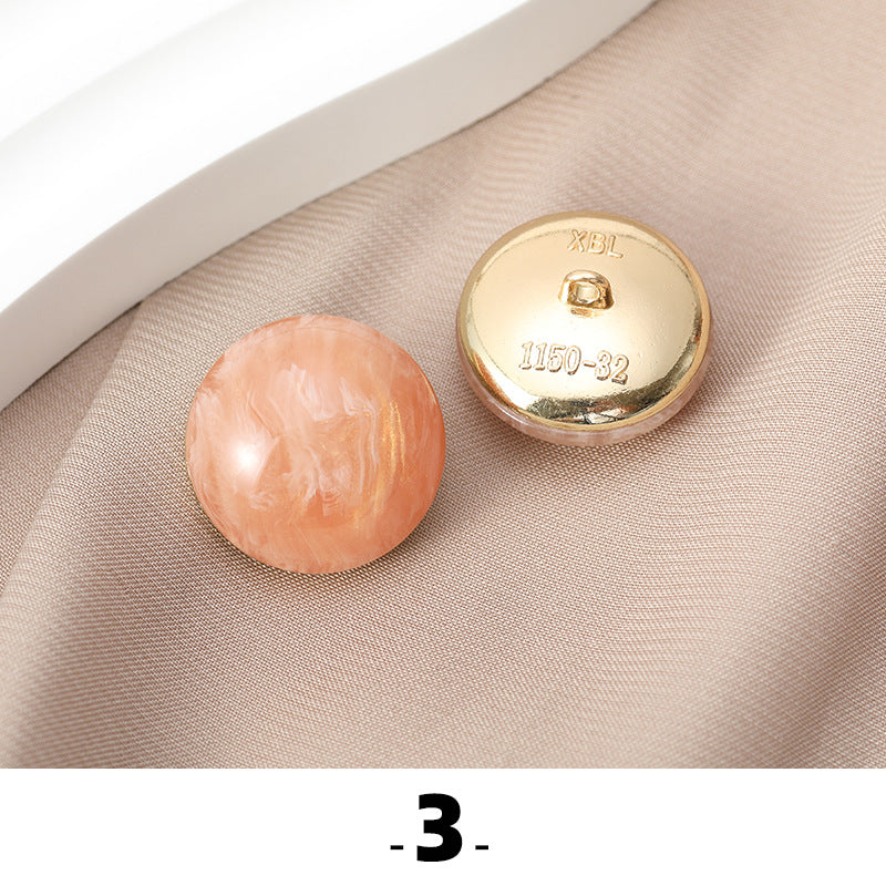 Peach cat’s eye resin button with gold metal base, back side facing up