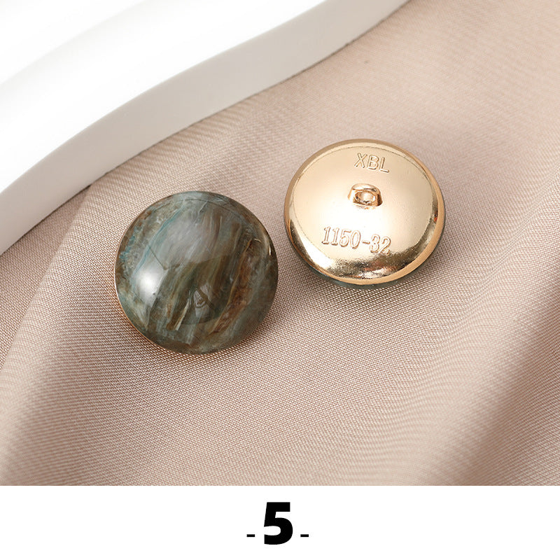 Green-gray cat’s eye resin button with gold metal base, back side facing up