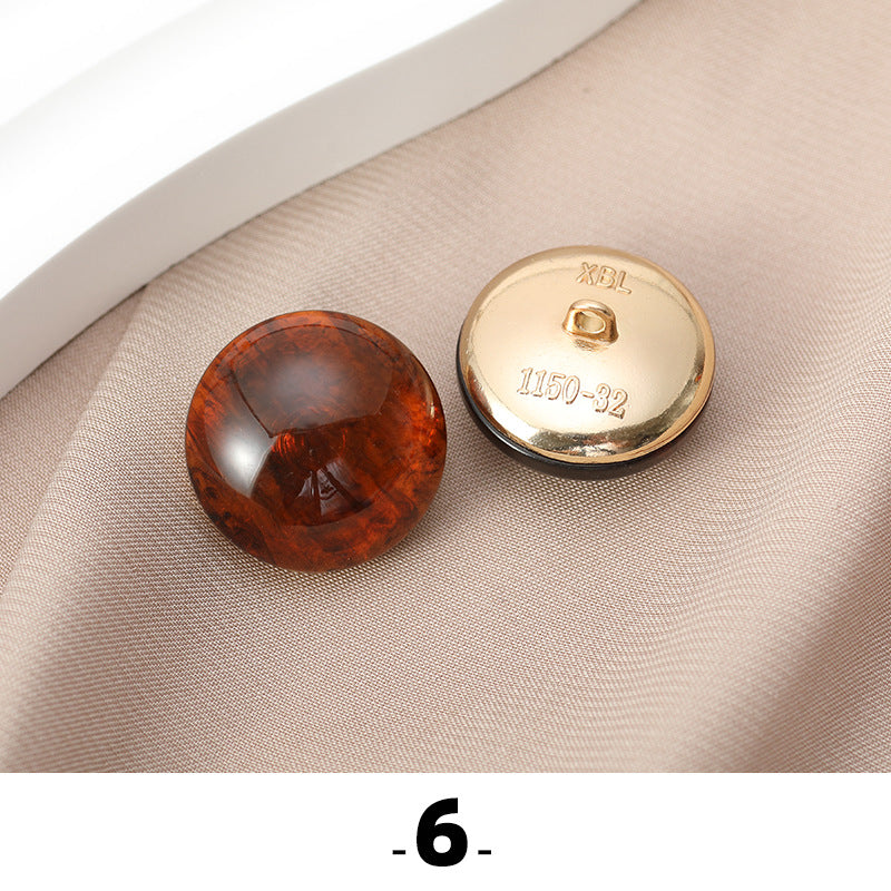 Rust-brown cat’s eye resin button with gold metal base, back side facing up