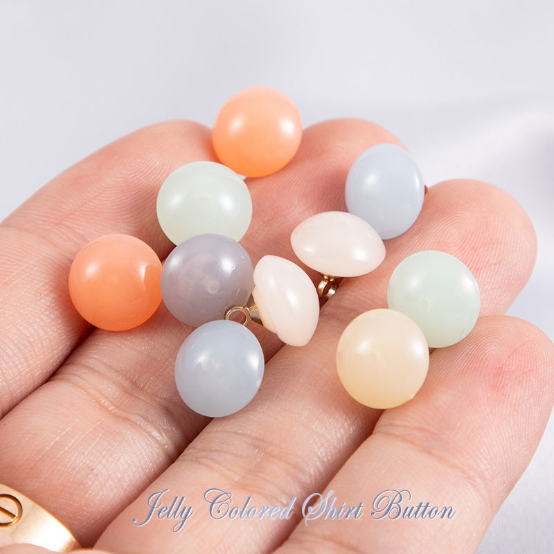 Assorted jelly-colored resin round shirt buttons held in hand, gold-tone shank backs