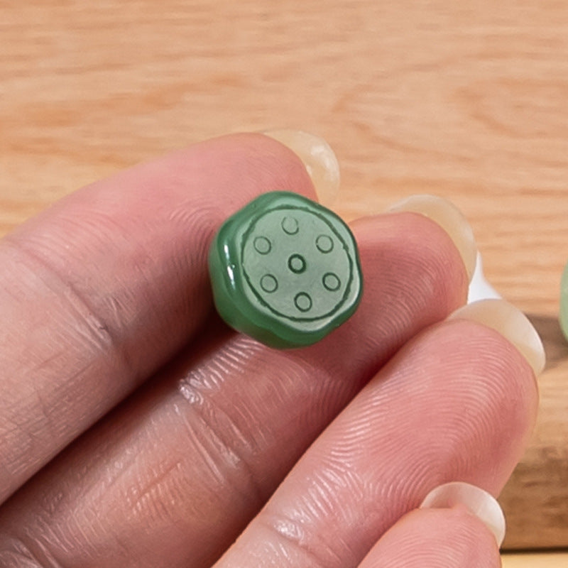 Nahaufnahme: grüner Glas-Lotusknopf mit Punktrelief, in der Hand gehalten