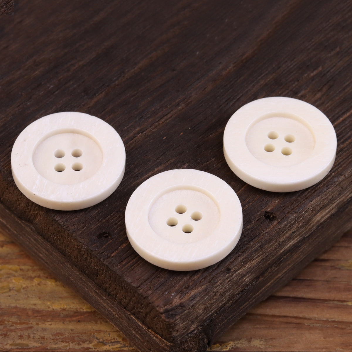 Wide-edged 4-hole bone buttons, light ivory, three-button arrangement close-up