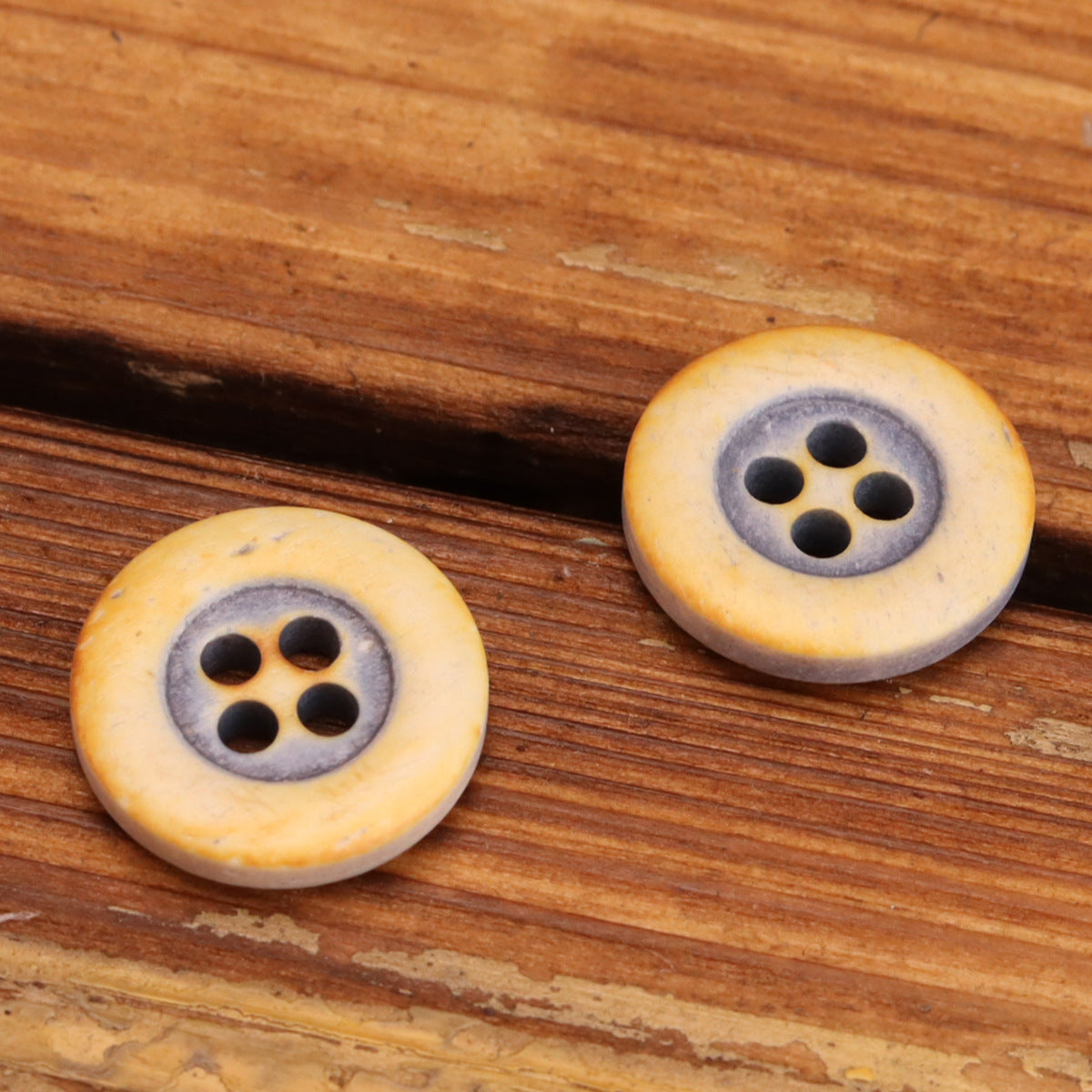 Two round 4-hole bovine bone buttons, warm yellow with gray ring, rounded edge