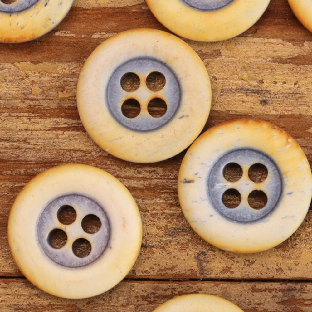 Multiple round 4-hole bovine bone buttons, warm yellow with gray rings, rounded edges